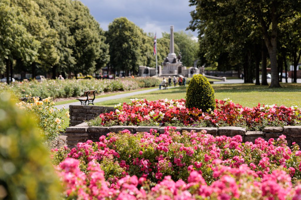 Borders of pink summer bedding plants surrounding the Diamond in Port Sunlight, with the War Memorial in the distance.